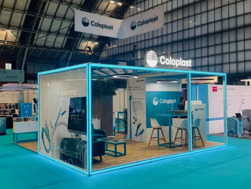 Wide-angle view of Coloplast’s illuminated 6m x 6m modular island stand at BAUS 2024, featuring an open-plan layout, edge-lit frame, and branded SEG graphics.